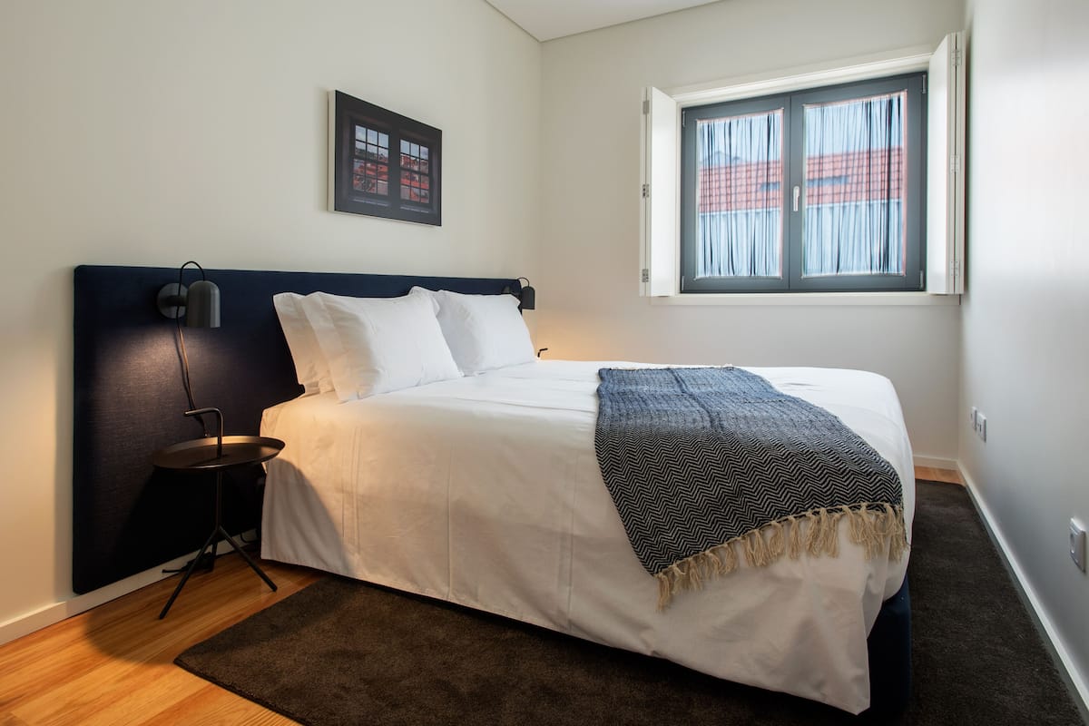 A neatly made bed with white linens, a dark headboard, and a grey herringbone throw blanket.