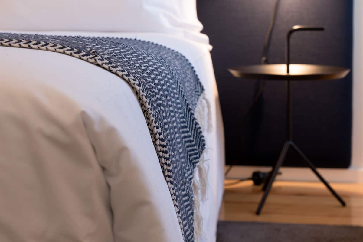 A neatly made bed with white and patterned linens, a dark headboard, and a small side table with a lamp.