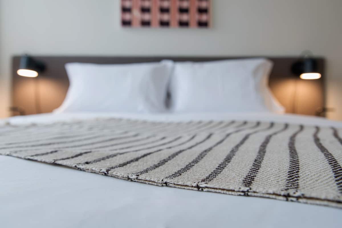 A bed with white linens and a striped area rug.
