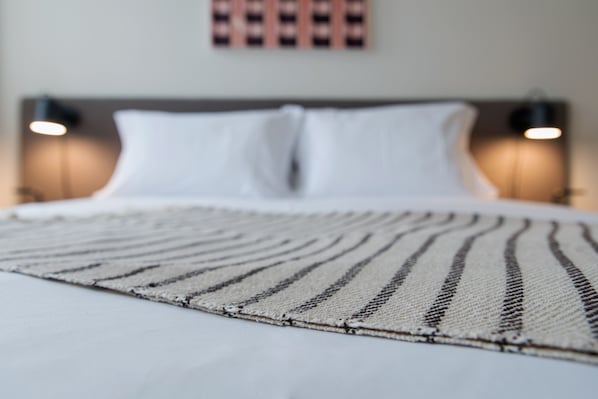 A bed with white linens and a striped area rug.