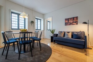 Uma sala de estar moderna com um sofá azul, uma mesa de jantar com cadeiras e uma janela grande com cortinas.