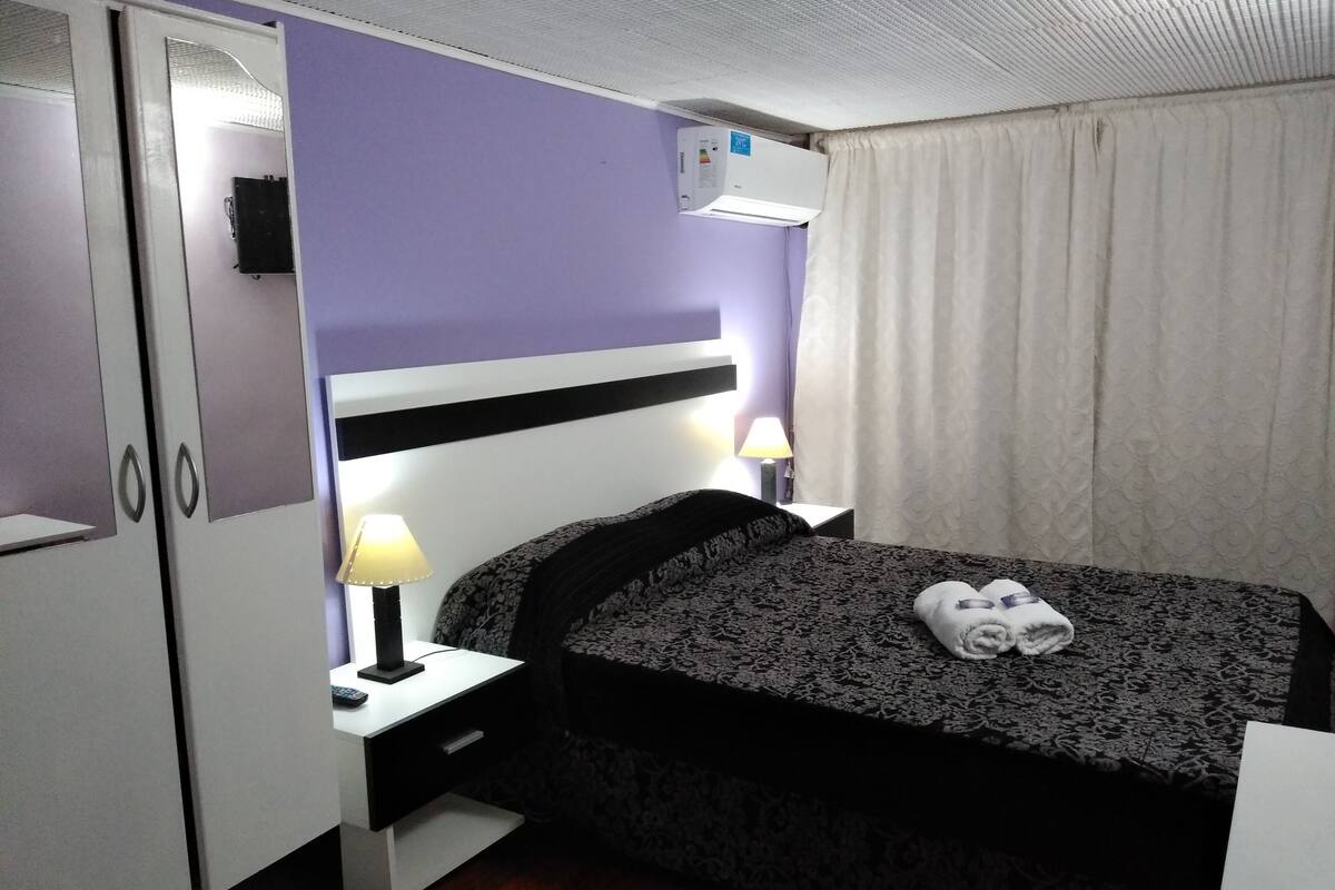 A hotel room with a bed, a desk, a wardrobe, and an air conditioning unit.