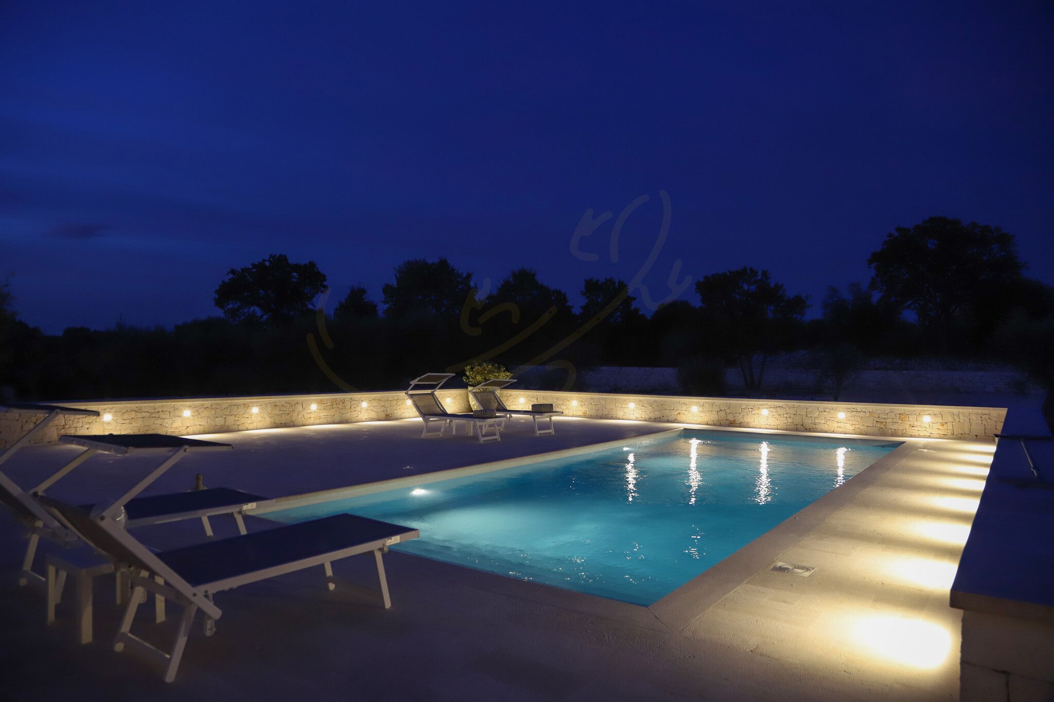 An outdoor swimming pool with a stone wall and lounge chairs.