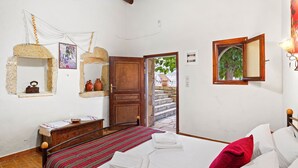Une chambre à coucher avec un lit, une porte en bois, une fenêtre donnant sur un paysage agréable et une étagère murale décorée de divers objets.