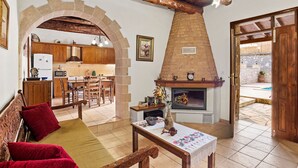 Un salon chaleureux avec une cheminée, des meubles en bois et une porte en arc donnant sur la cuisine.