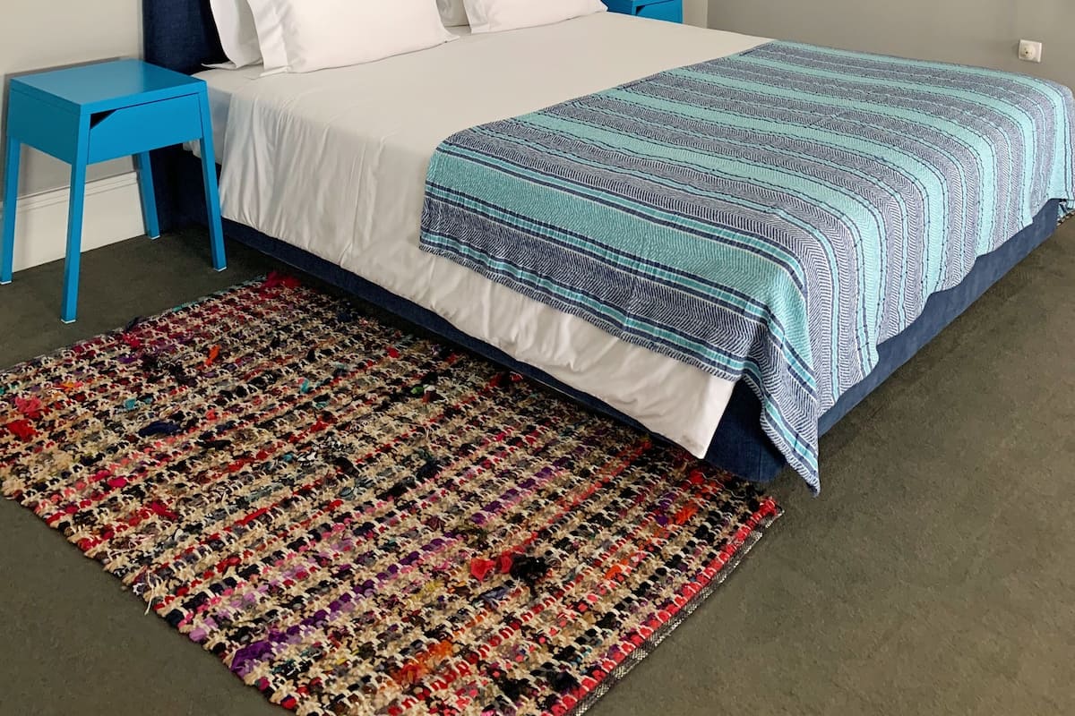 A bedroom with a bed, a blue headboard, white bedding, a colorful rug, and two nightstands with wall-mounted lamps.