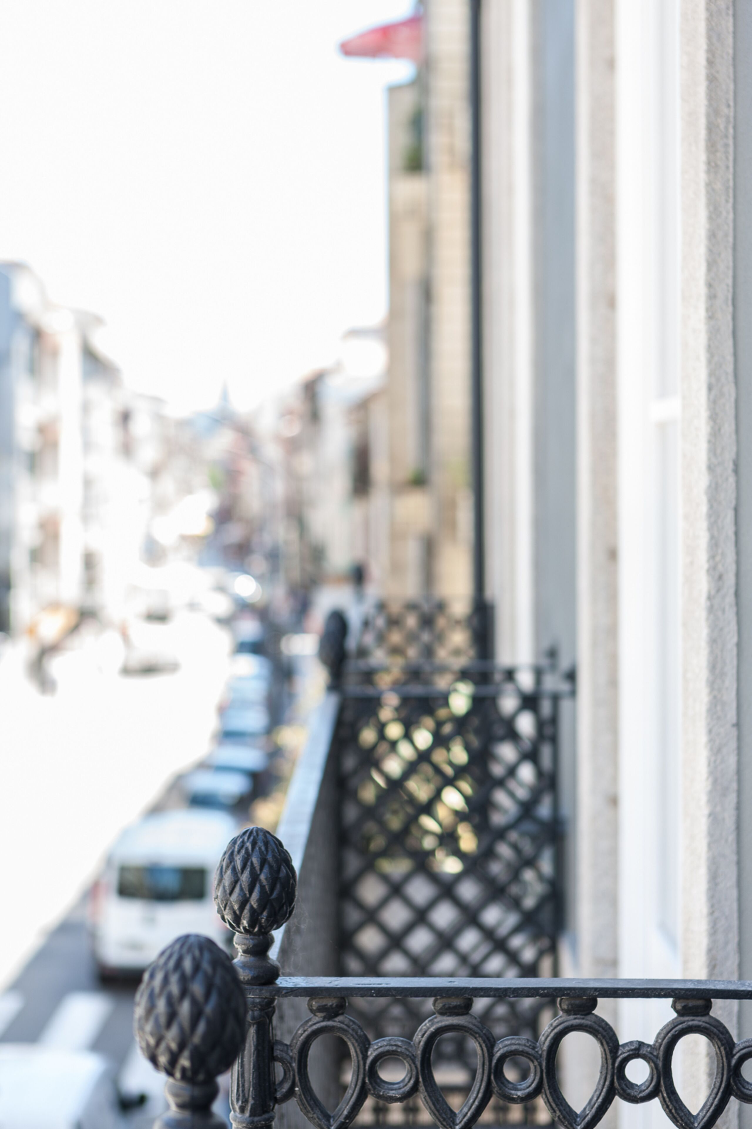 Un balcone con ringhiera in ferro battuto e vista su una strada con auto parcheggiate e palazzi.