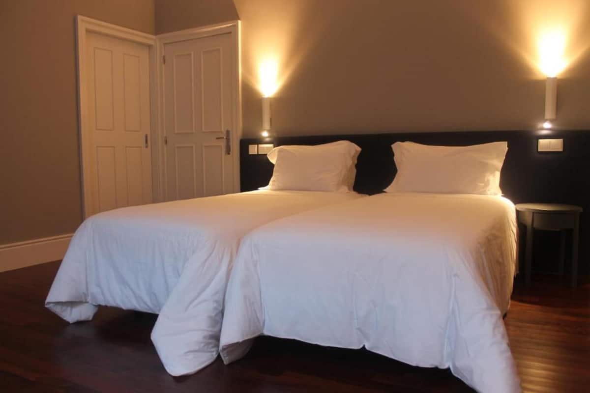 A double bed with white bedding in a room with wooden flooring and two wall-mounted lights.
