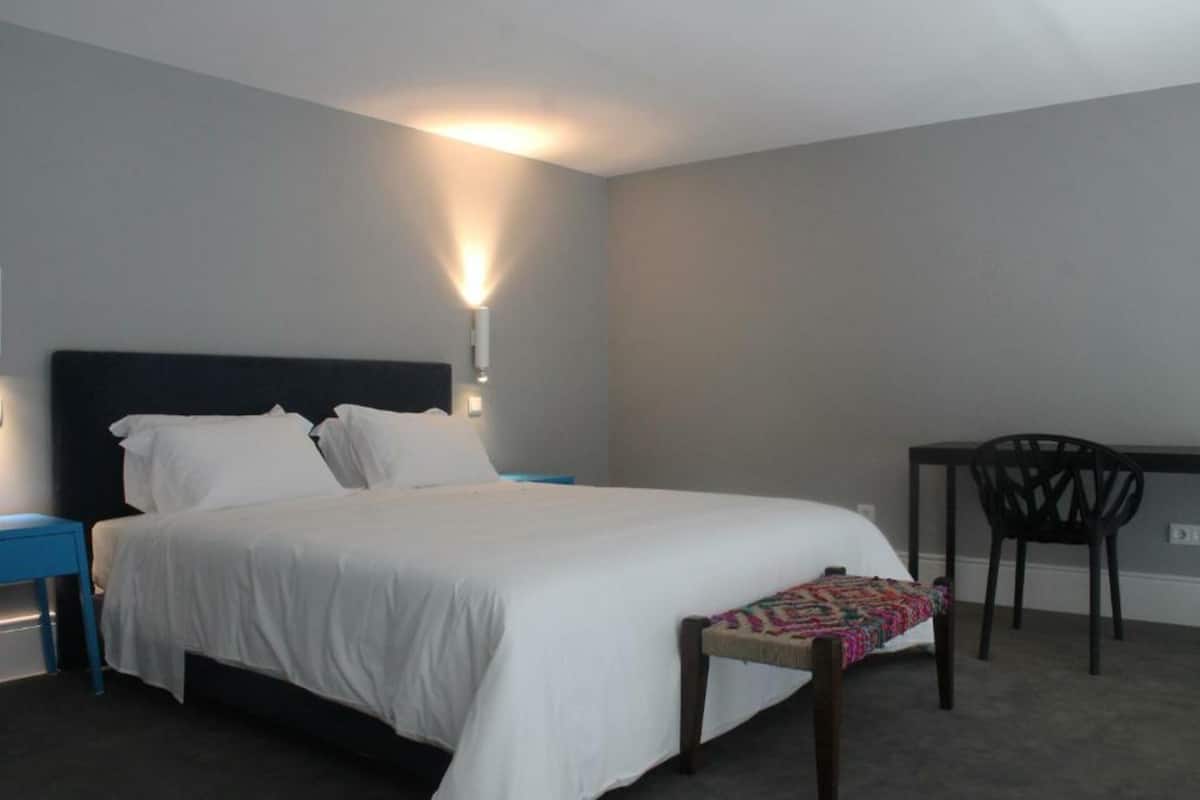 A neatly made bed with white linens, a blue bedside table, and a chair with a colorful cushion.