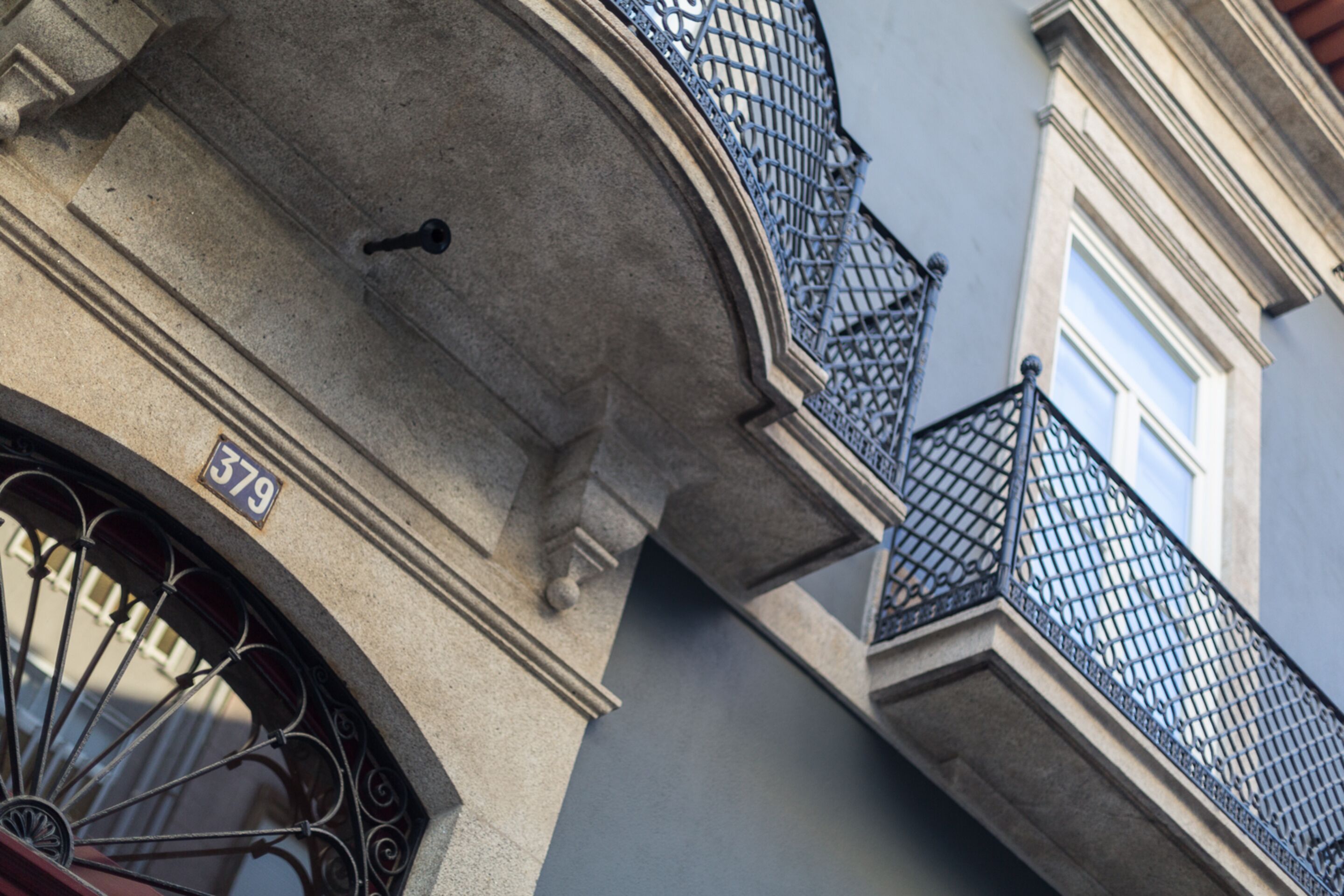 Fachada de edificio con balcón de hierro forjado y marco de piedra.