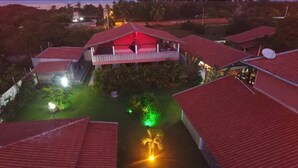 A hotel with multiple red-roofed buildings, a central structure with a balcony, and a well-maintained garden area with green lighting. - Paracuru Kitefriends Pousada (Paracuru)