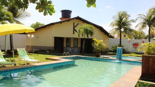 A swimming pool with lounge chairs and a building with a large 'K' on the facade. - Paracuru Kitefriends Pousada (Paracuru)