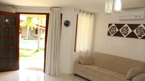 A living room with a beige sofa, a clock on the wall, and a view of a pool outside. - Paracuru Kitefriends Pousada (Paracuru)