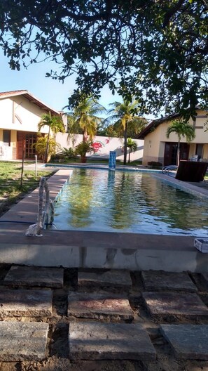 A swimming pool with a stone border, surrounded by palm trees and buildings. - Paracuru Kitefriends Pousada (Paracuru)