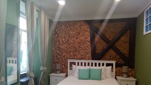 A bedroom with a bed, two bedside tables, a window with curtains, and a textured wall.