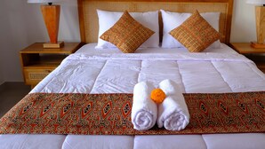 A neatly made bed with white linens, two decorative pillows, a folded towel, and a patterned throw blanket. - Bale Delod Guest House (Ubud)