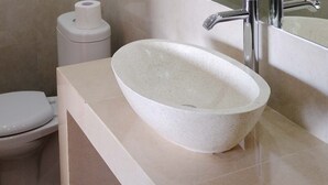 A bathroom with a white toilet, a white sink with a speckled design, and a toilet paper holder. - Bale Delod Guest House (Ubud)
