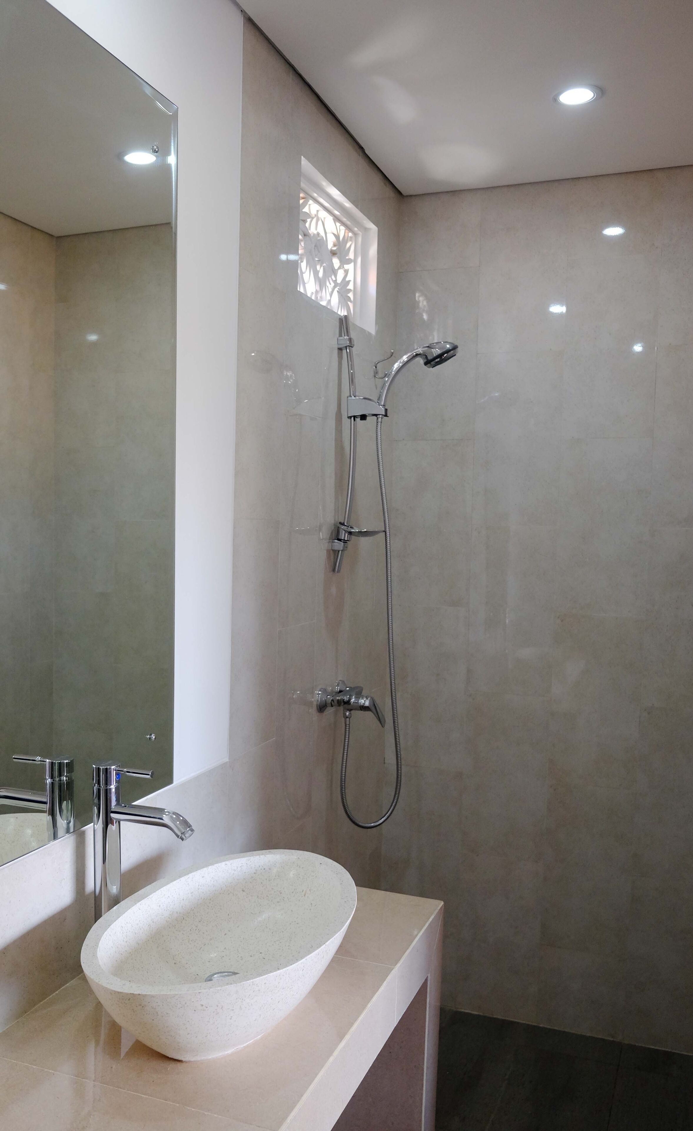 A modern bathroom with a large mirror, a white sink, and a shower with a handheld showerhead.