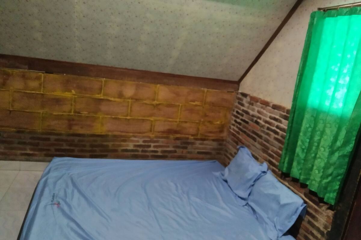 A room with a brick-patterned headboard, a bed with blue bedding, and a green curtain.