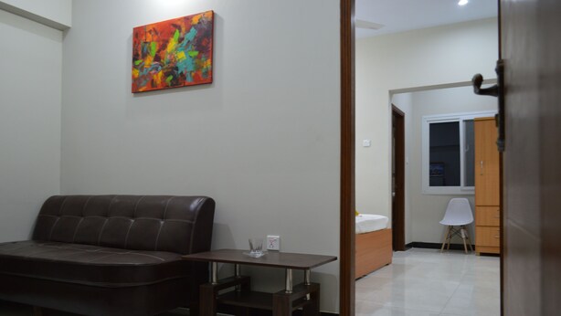 Uma sala de estar com um sofá de couro marrom, uma mesa de madeira pequena e um quadro abstrato colorido na parede.