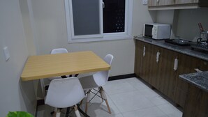Uma cozinha pequena com uma mesa de madeira e duas cadeiras brancas, micro-ondas e fogão.