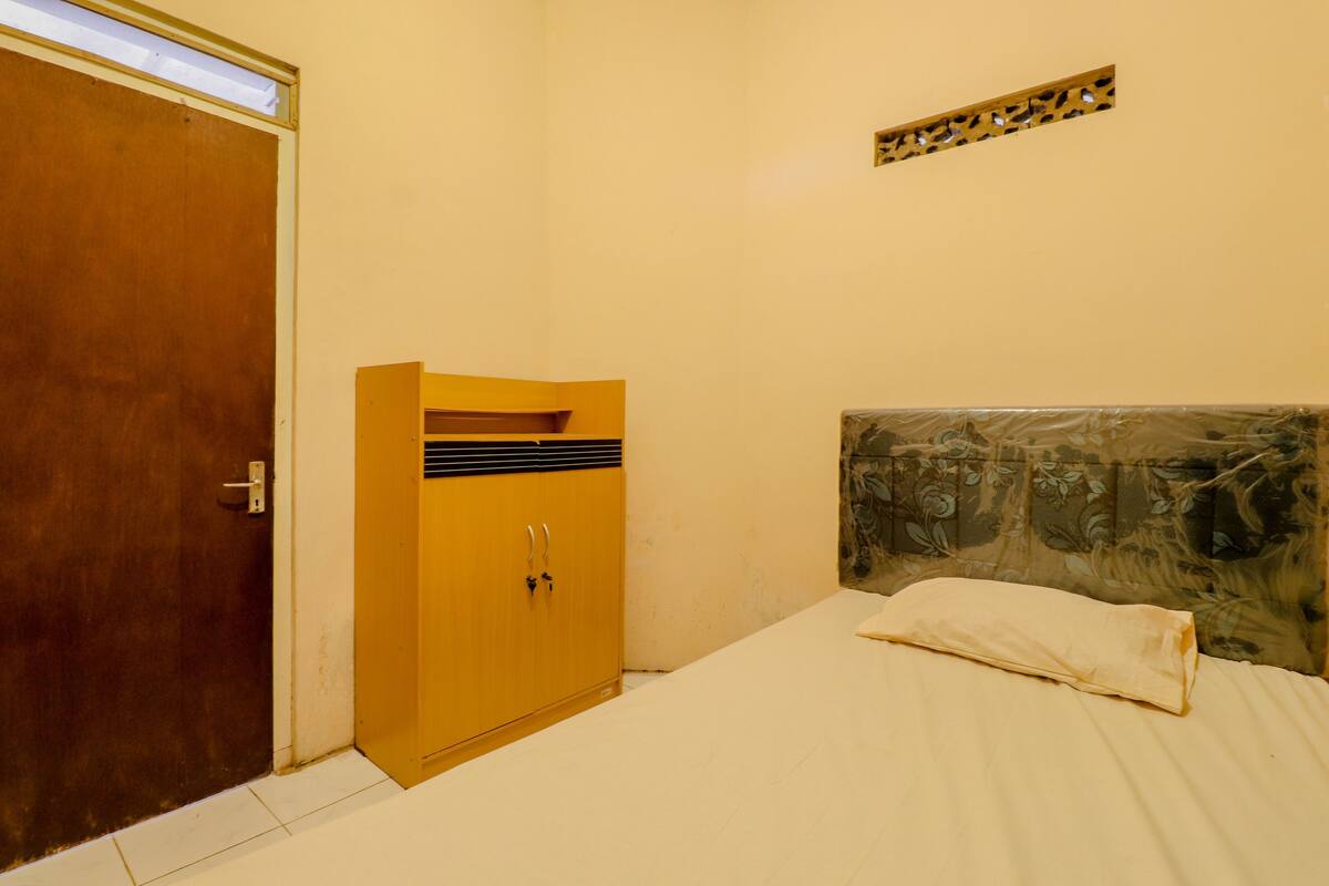 A room with a wooden wardrobe, a bed with a patterned headboard, and a small decorative panel on the wall.