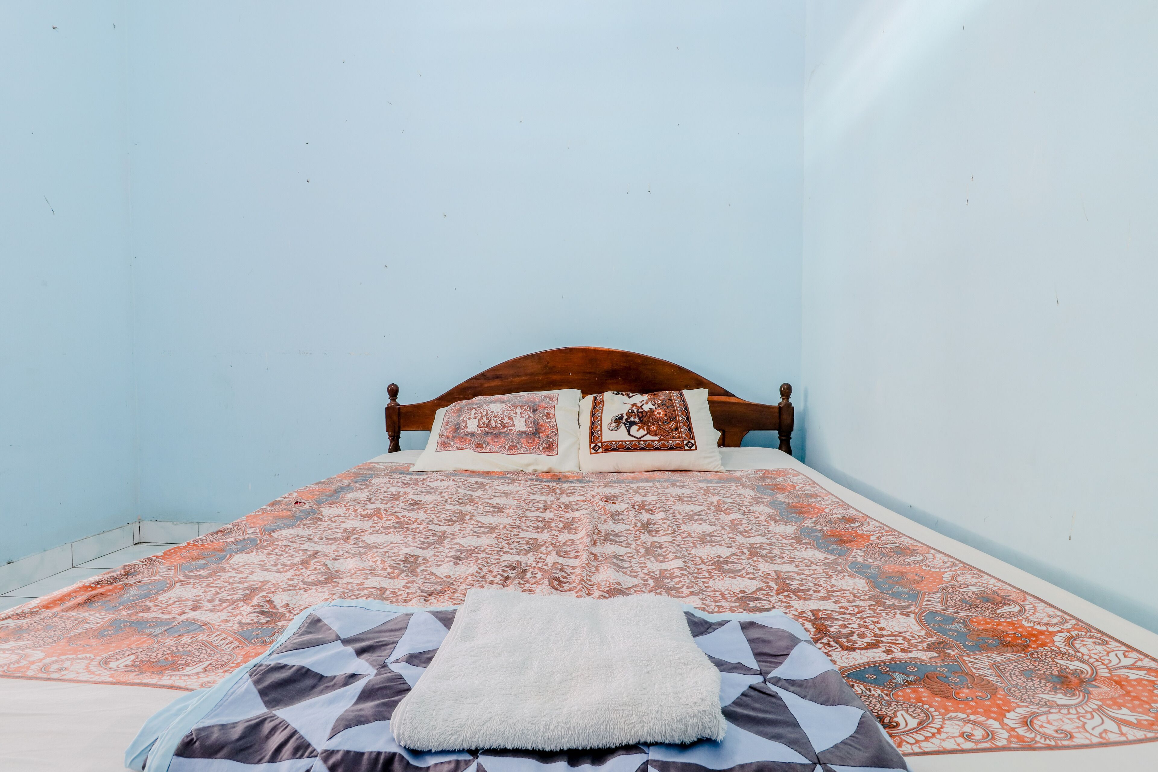 Una habitación pequeña con cama individual, cabecera de madera, colcha estampada y una manta blanca.