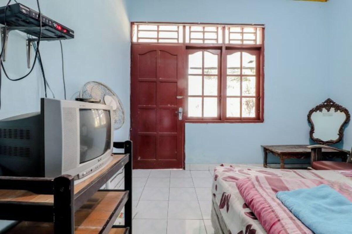 A bedroom with a bed, a TV, a wooden cabinet, a window, and a door.