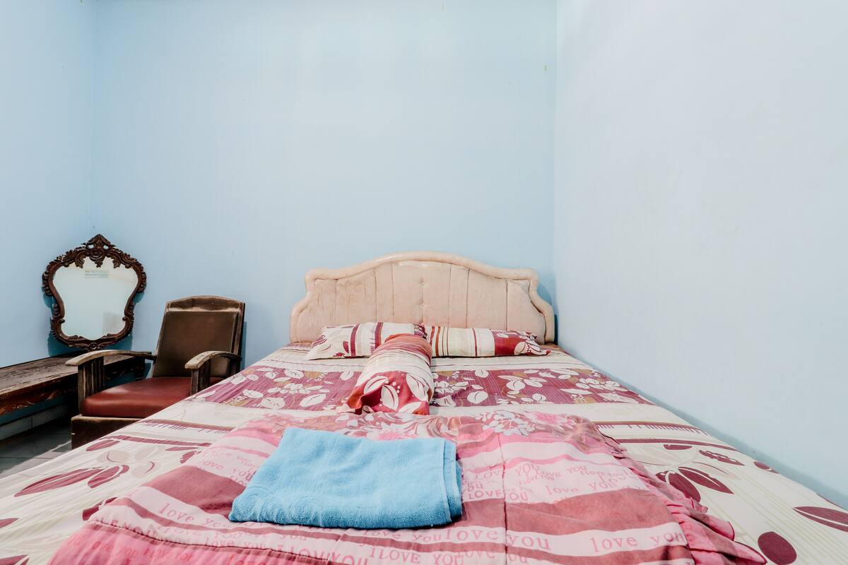A bedroom with a bed, a chair, a wooden bench, and a mirror on the wall.