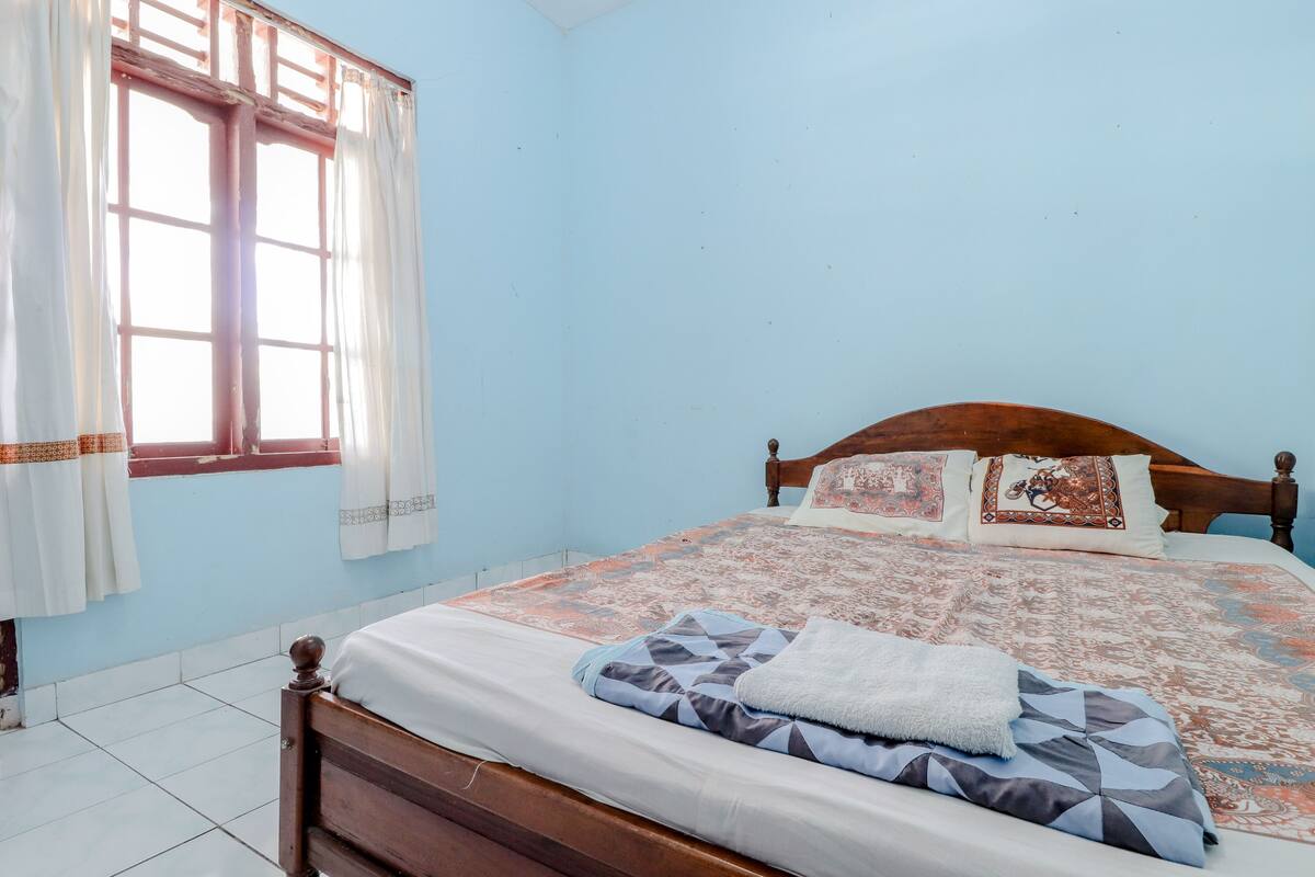 A bedroom with a wooden bed, patterned bedding, and a window with curtains.