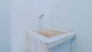 A bathroom with a white tiled floor and walls, a small window, and a faucet. - Losmen Parikesit (Parangtritis)