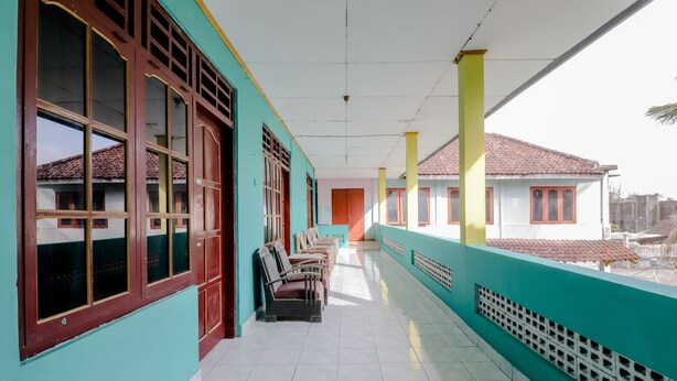 A corridor with teal walls, wooden-framed windows, and a tiled floor. - Losmen Parikesit (Parangtritis)