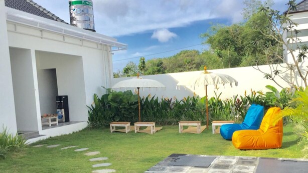 Un jardin avec une piscine, un espace salon extérieur et un bâtiment blanc surmonté d’un réservoir d’eau.
