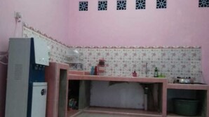 Une petite cuisine avec un mur rose, un réfrigérateur, un évier et un plan de travail sur lequel se trouvent divers objets.
