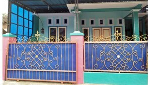 Un bâtiment à deux étages, à la façade bleue et rose, doté d’un portail en métal orné de motifs décoratifs et d’un porche abrité.