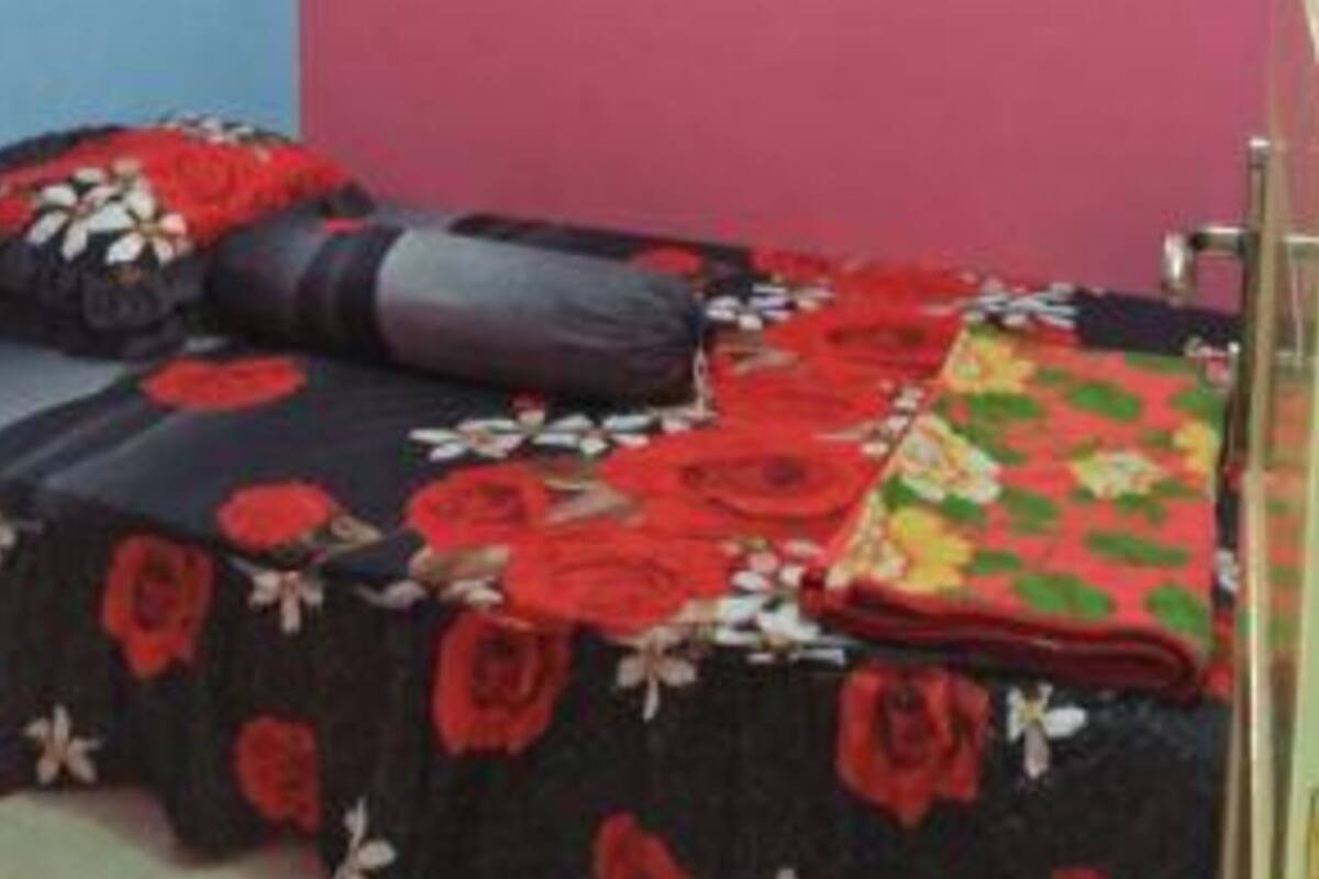 A room with a bed covered in floral bedding, a pink wall, and a small framed picture.