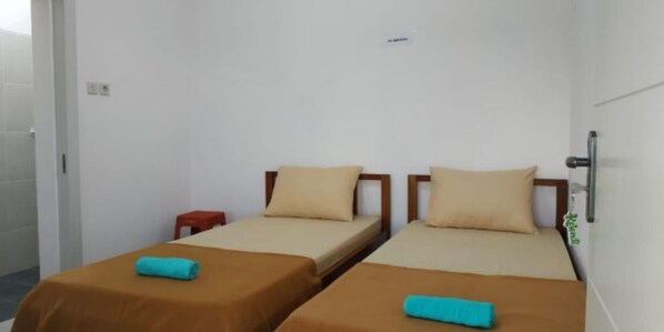 A room with two single beds, each with a brown bedspread and a blue towel. There is a small red stool and a white wall with a sign above the beds. - Sunrise of Java (Banyuwangi)