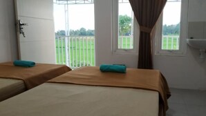 Quarto com duas camas, janela com vista para um campo verde, banheiro com pia e porta com fechadura.