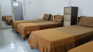Quarto de dormitório com várias camas individuais, cada uma com cobertura marrom, e um armário alto com vários compartimentos.