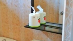 Um banheiro com vaso sanitário, pia e espelho sobre a pia. Há duas caixas de lenços de papel em uma prateleira acima da pia.