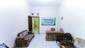 Zona de recepción con mostrador, dos sofás de madera, una mesa de madera y suelo de baldosas.