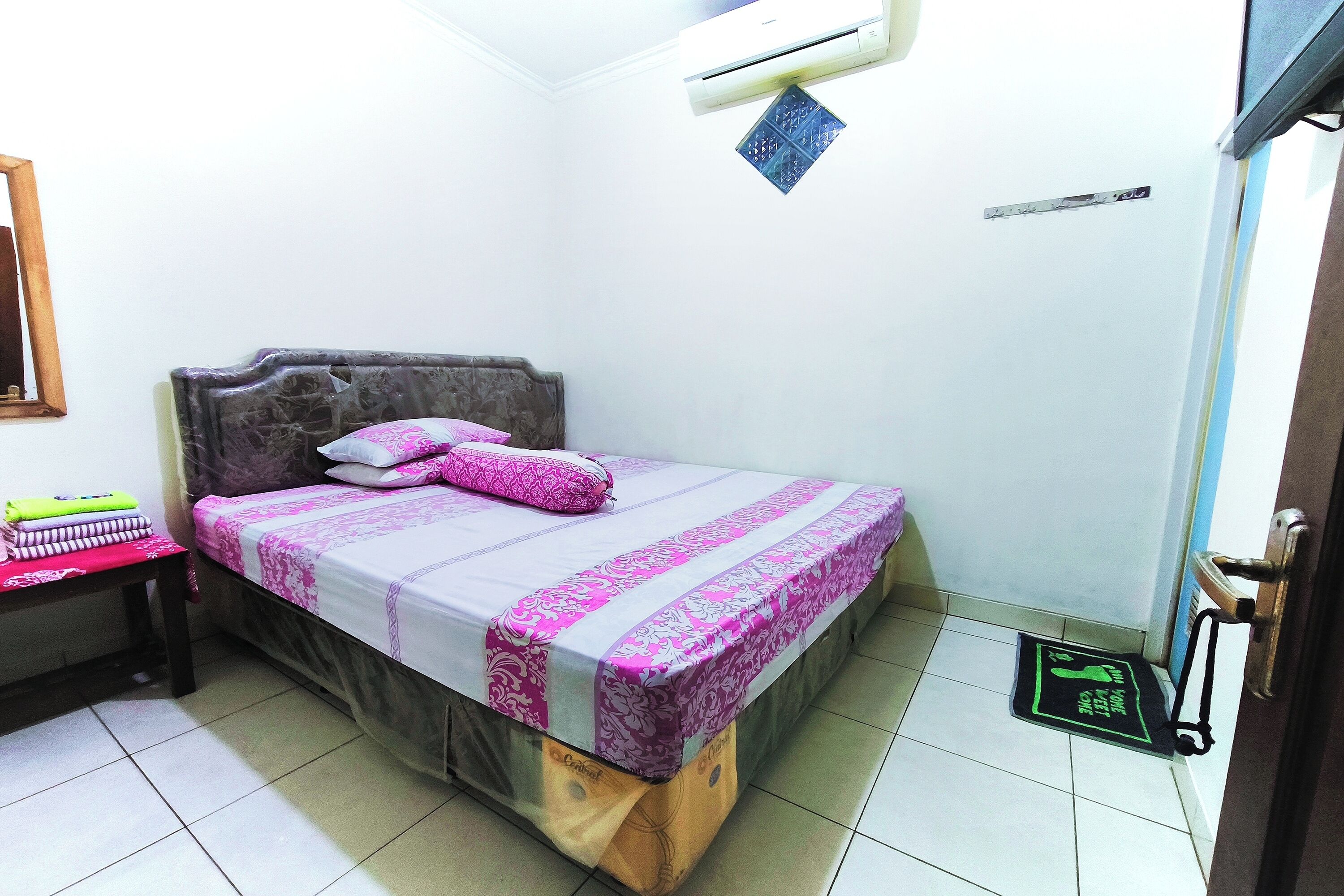 Un dormitorio con una cama, una mesita de noche, una puerta y un aire acondicionado instalado en la pared.
