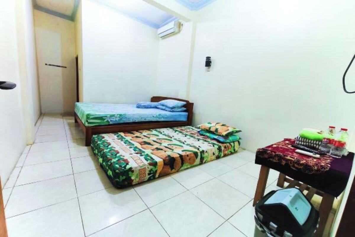 Una habitación pequeña con una cama, una mesa y objetos, y una puerta.
