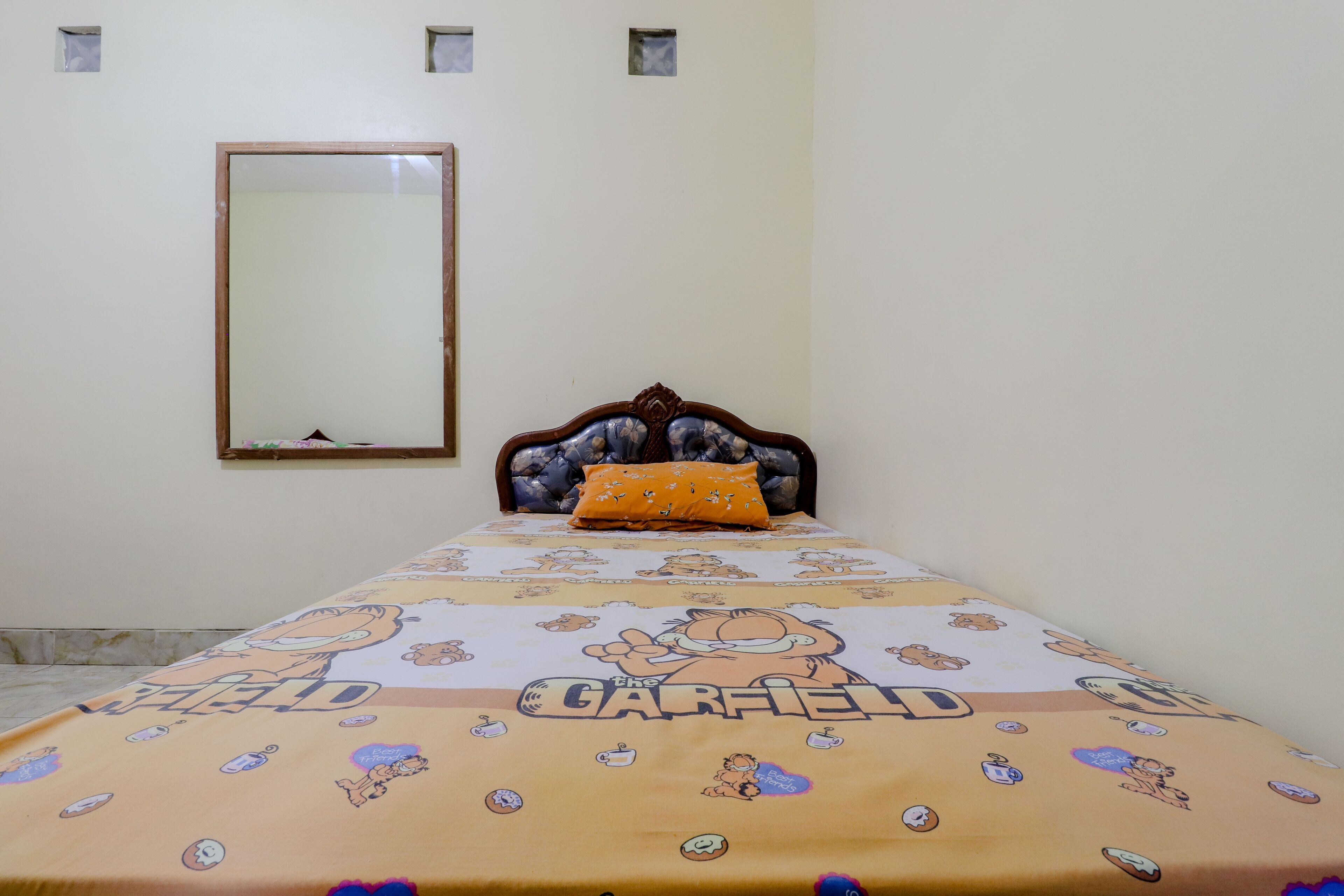 A bedroom with a single bed, a wooden headboard, a mirror on the wall, and a Garfield-themed bedspread.