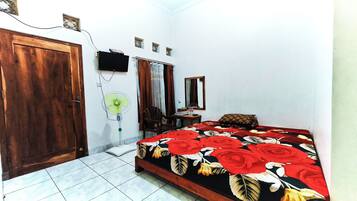 A bedroom with a bed, a wooden door, a wall-mounted TV, a small table, and a chair.