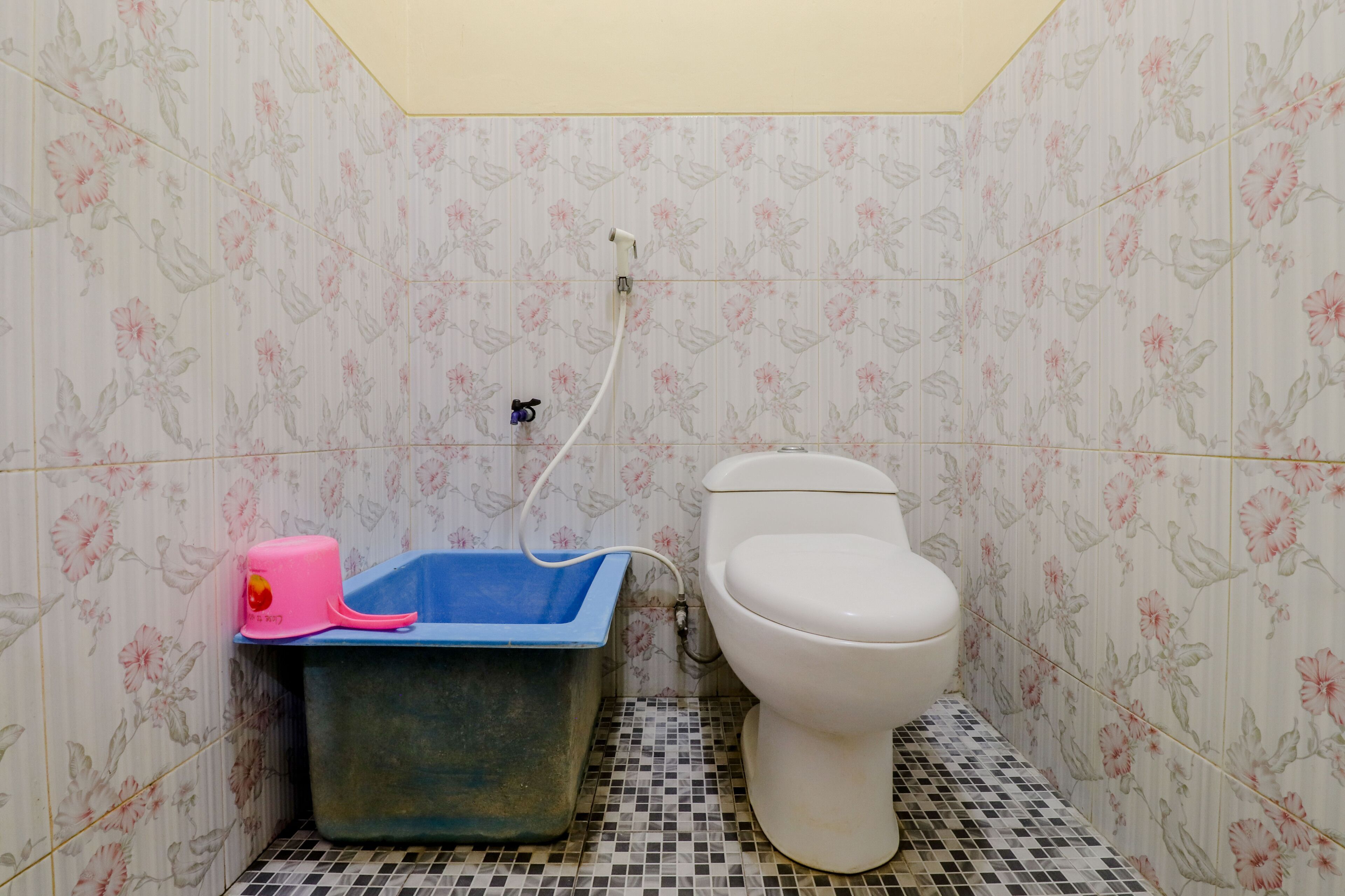A bathroom with a toilet, a blue bucket, and a pink tissue dispenser.