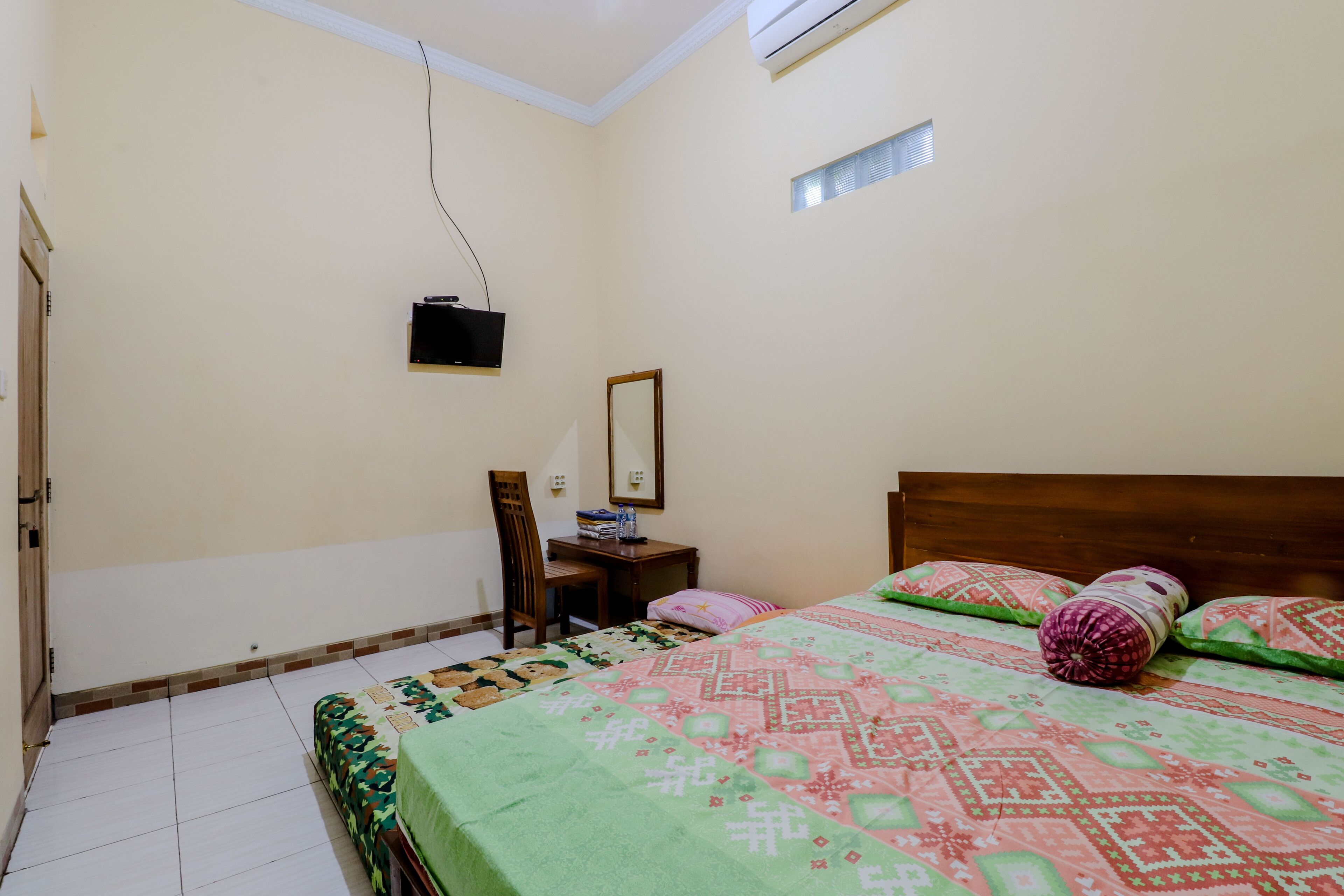 A bedroom with a bed, a desk, a chair, and a television mounted on the wall.
