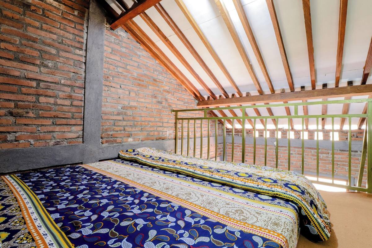 A room with a brick wall, a wooden ceiling, and a bed with patterned bedding.