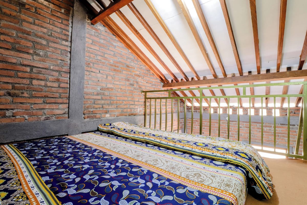 A room with a brick wall, a wooden ceiling, and a bed with patterned bedding.