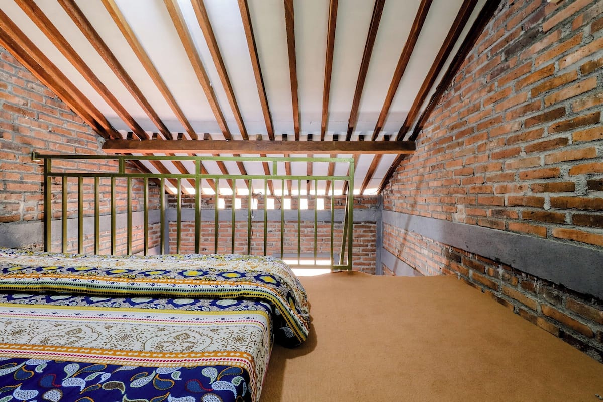 A room with a sloped ceiling, exposed wooden beams, a brick wall, and a bed with patterned bedding.